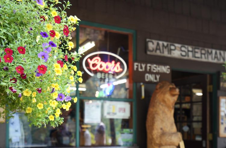 hanging flower basket in front of a small store with a wooden bear statue