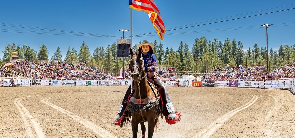 girl on horse holding American flag at sisters rodeo